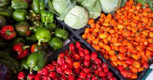 A vibrant display of fresh vegetables including peppers and cabbage at an outdoor market.